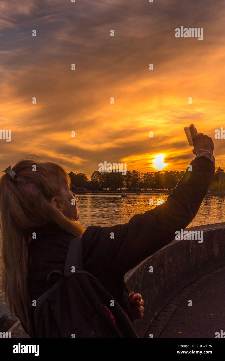 Femme adulte prenant un selfie le soir avec le lac en arrière-plan. Banque D'Images