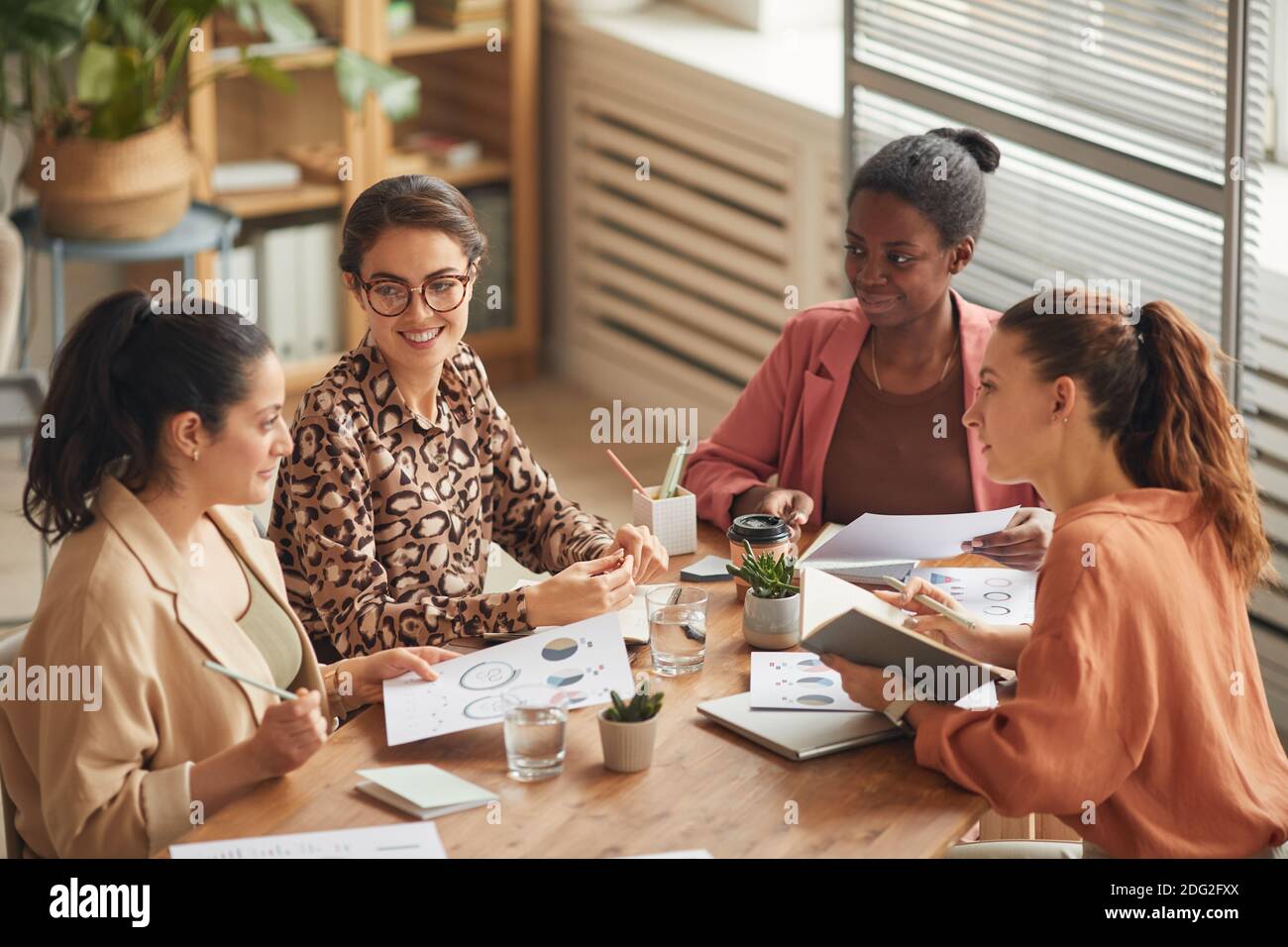 Portrait en grand angle d'une équipe d'affaires féminine réussie discutant du travail à la table de réunion et souriant gaiement, espace de copie Banque D'Images