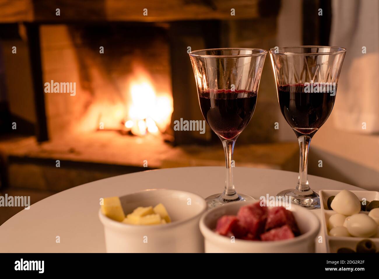deux verres de vin, fromage, salami, olives et œufs de caille devant une cheminée Banque D'Images deux verres de vin, fromage, salami, olives et œufs de caille devant une cheminée Banque D'Images