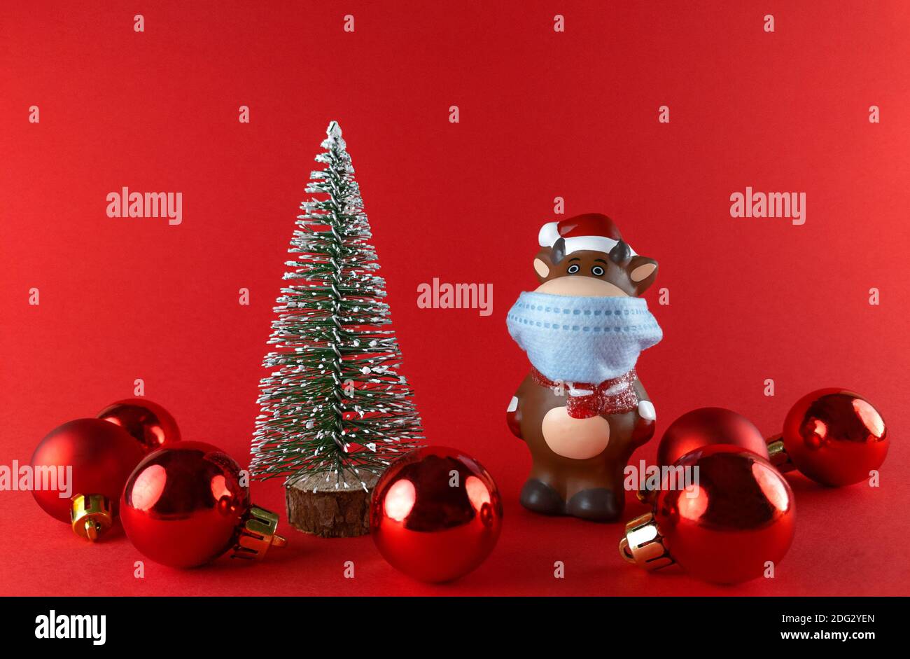 Statuette en céramique d'Ox dans un masque médical, un arbre de Noël et des boules sur un arrière-groupe rouge. Symbole du nouvel an 2021. Banque D'Images