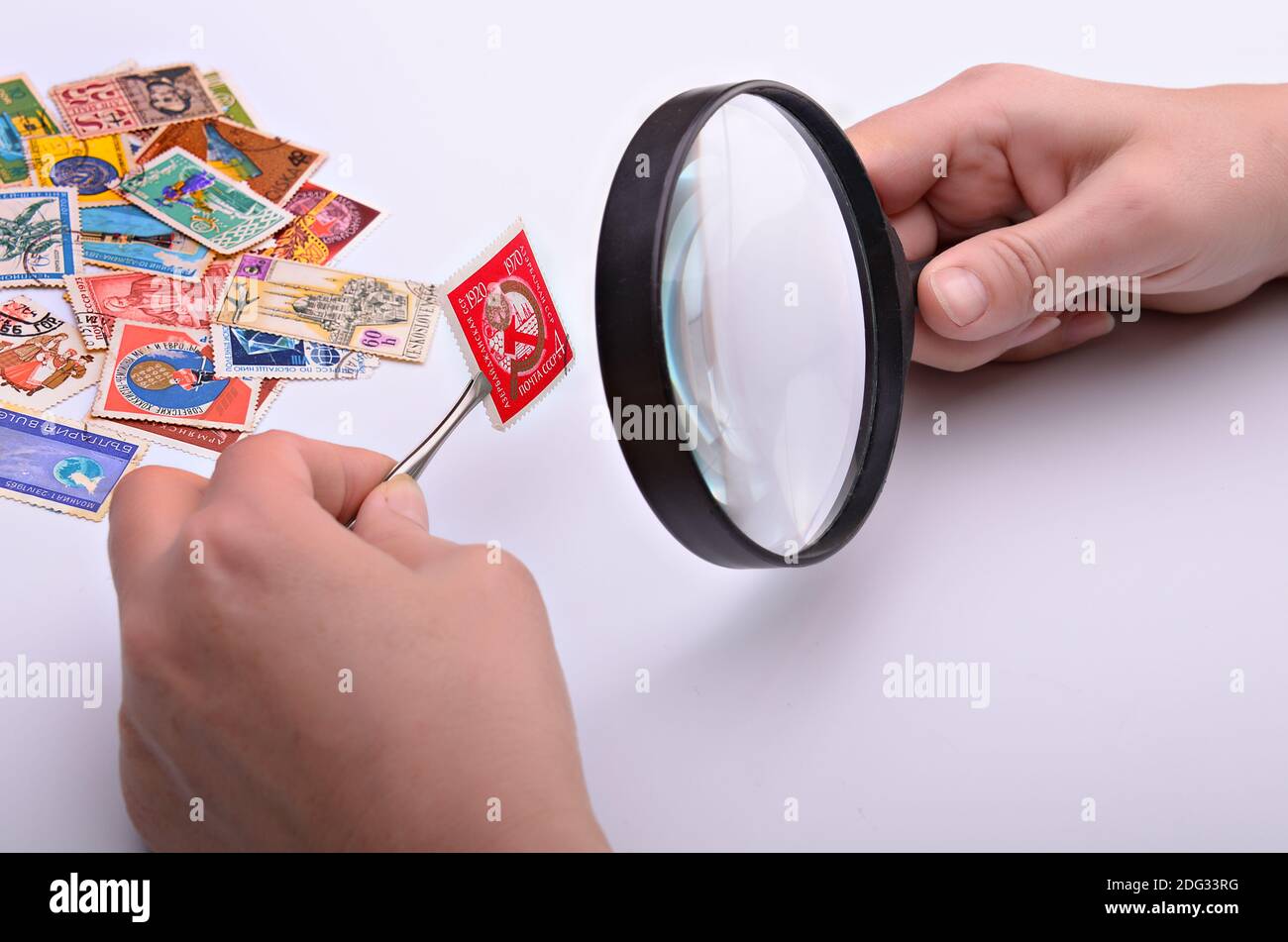 Ancien timbre entre les mains de la philatéliste avec une loupe sur un arrière-plan clair Banque D'Images