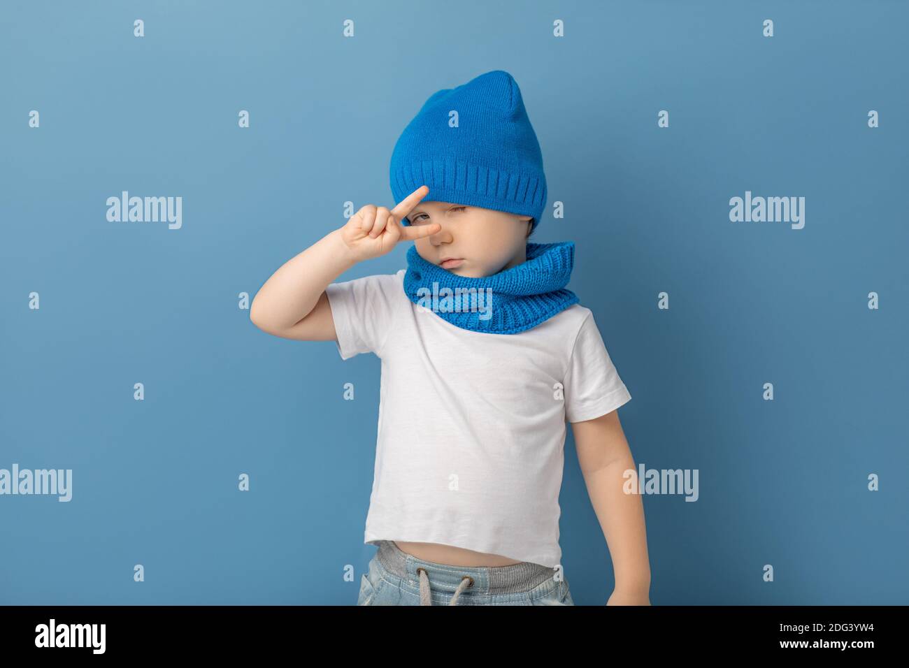 Enfant garçon avec les doigts montre signe geste selfie, victoire, symbole de paix et de patséphisme. Gros plan en studio avec chapeau bleu et écharpe tube Banque D'Images