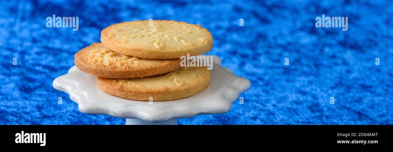 Biscuits de sucre estampés au flocon de neige frais cuits sur une céramique blanche présentoir à gâteaux et fond bleu Banque D'Images