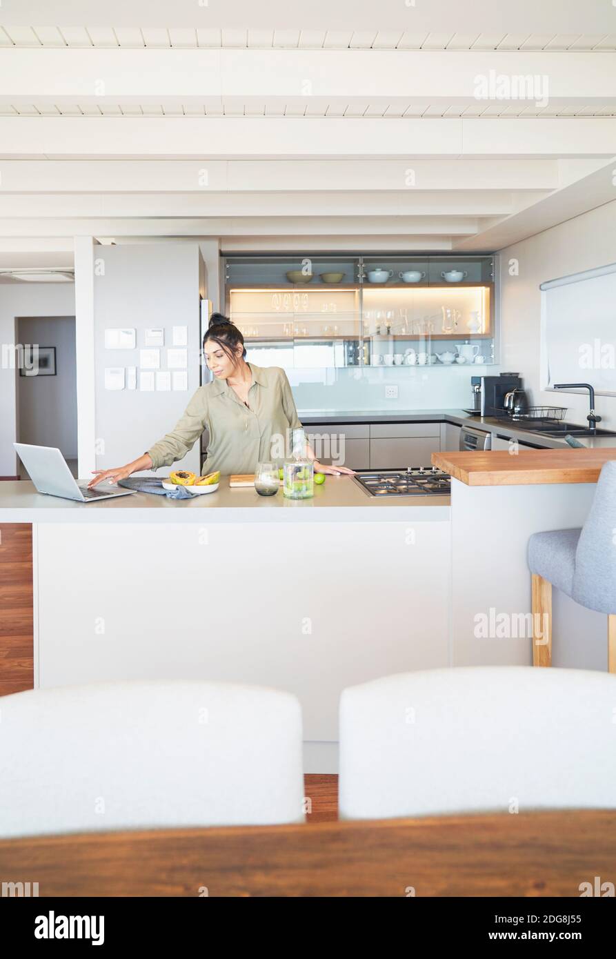 Femme avec un ordinateur portable travaillant et cuisinant dans une cuisine moderne Banque D'Images