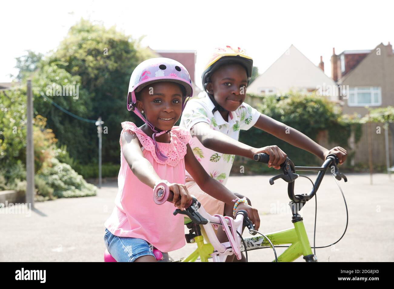 Portrait heureux frère et sœur à vélo dans un quartier ensoleillé Banque D'Images