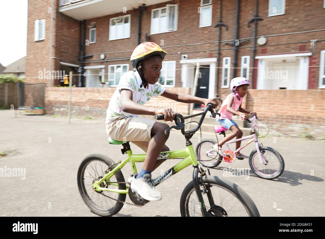 Frère et sœur à vélo dans un quartier ensoleillé Banque D'Images