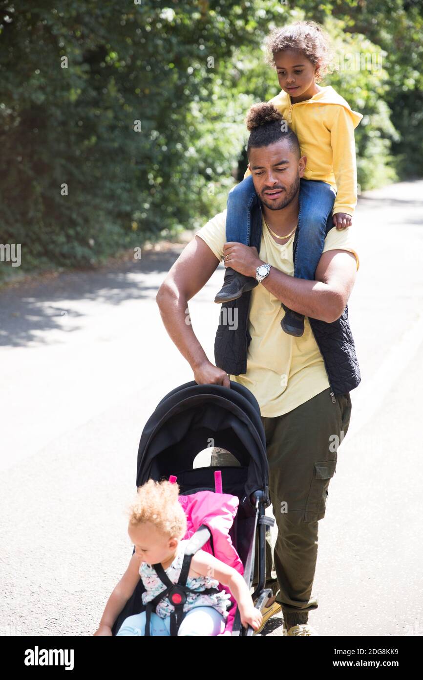 Père transportant et poussant sa fille dans une poussette sur un chemin ensoleillé Banque D'Images