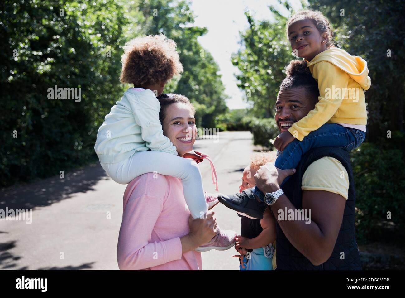 Portrait couple heureux portant des filles sur les épaules sur la route ensoleillée Banque D'Images