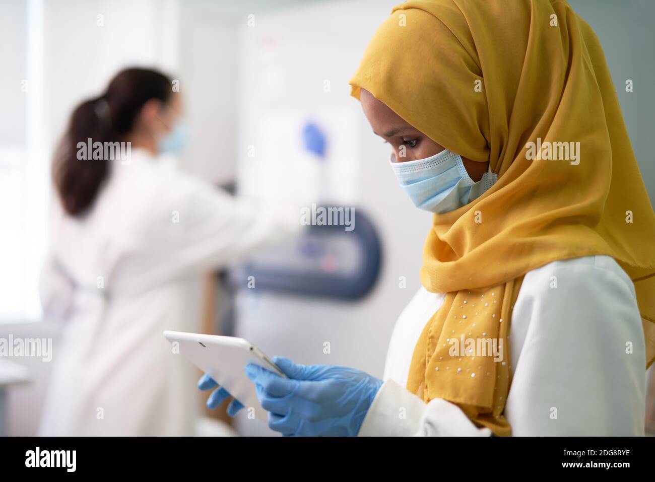 Scientifique féminine en hijab et masque facial en utilisant une tablette numérique Banque D'Images