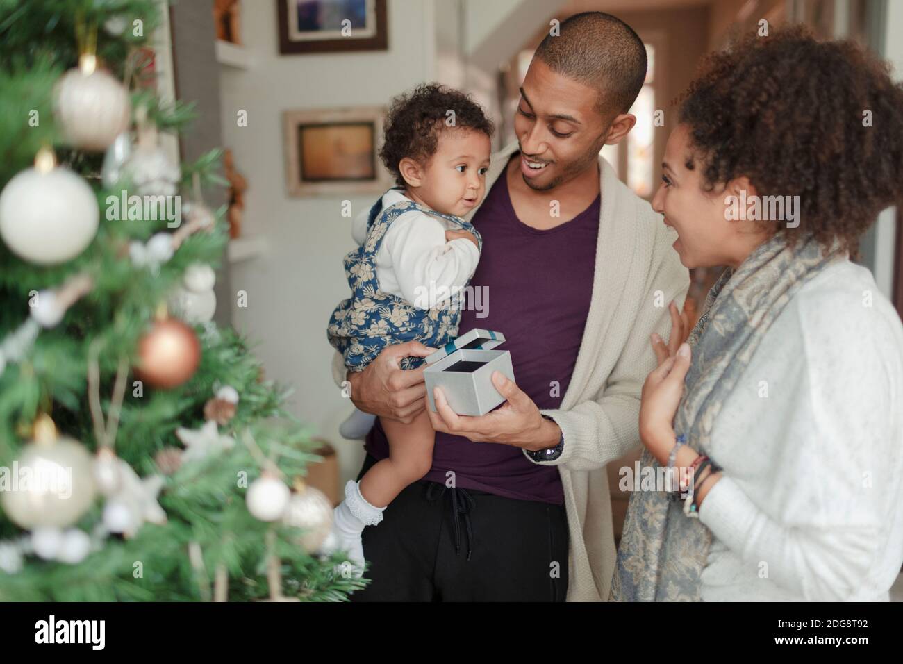 Parents heureux et bébé fille ouvrant des cadeaux de Noël par arbre Banque D'Images