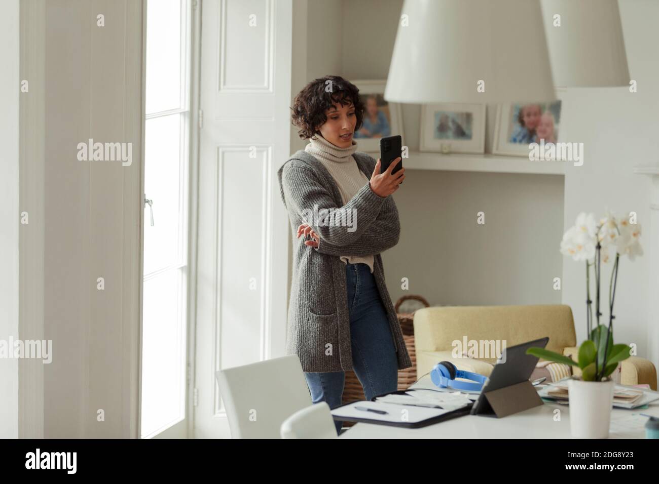 Femme avec smartphone travaillant à la maison à la fenêtre Banque D'Images