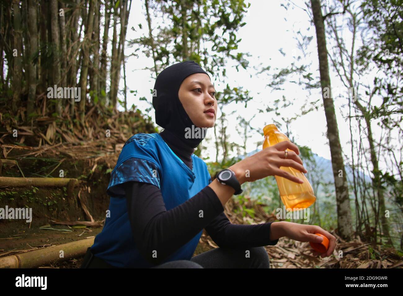 Attirante sportive asiatique musulmane portant le hijab à l'extérieur, assis, de l'eau potable Banque D'Images