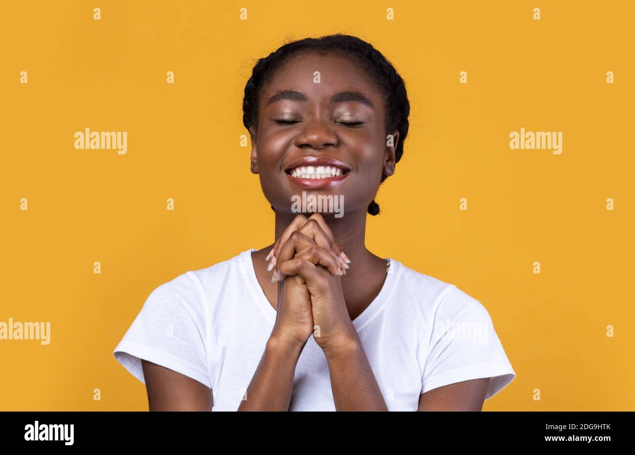 Femme noire priant en tenant les mains dans le geste de prière, fond jaune Banque D'Images