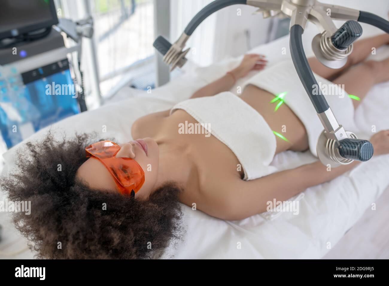 Jeune fille couché sous laser vert dans le centre de beauté Banque D'Images