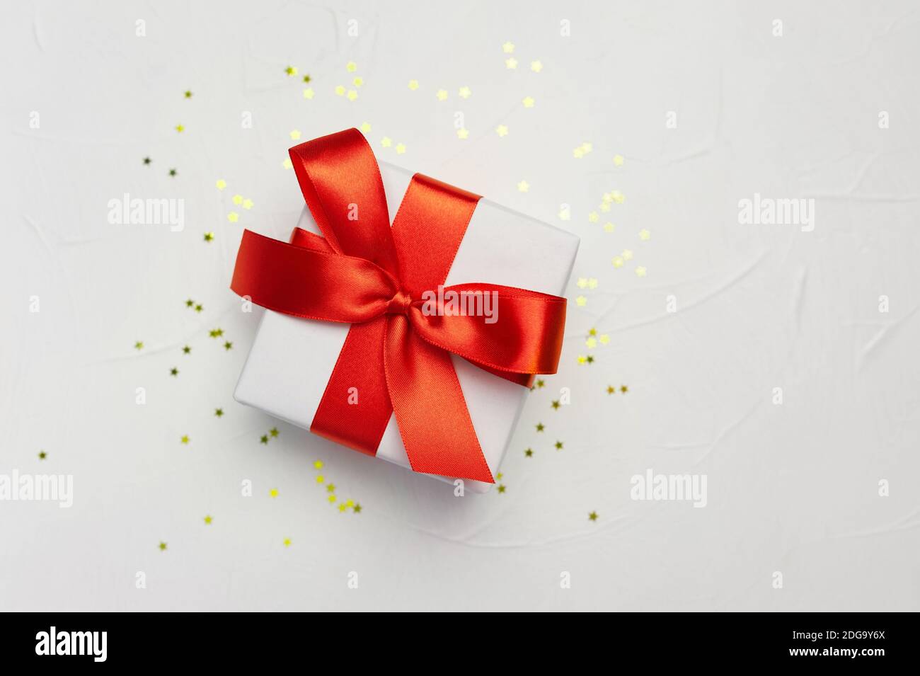 Boîte cadeau blanche décorative avec grand noeud rouge sur fond blanc et petites étoiles dorées. Modèle de carte de vœux avec emplacement pour le texte Banque D'Images