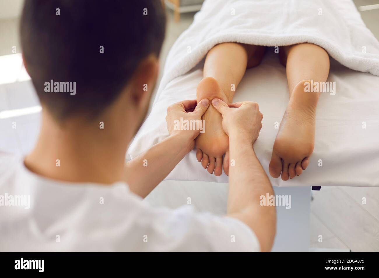Homme masseuse médecin en uniforme blanc massant les patients couchés talons Banque D'Images