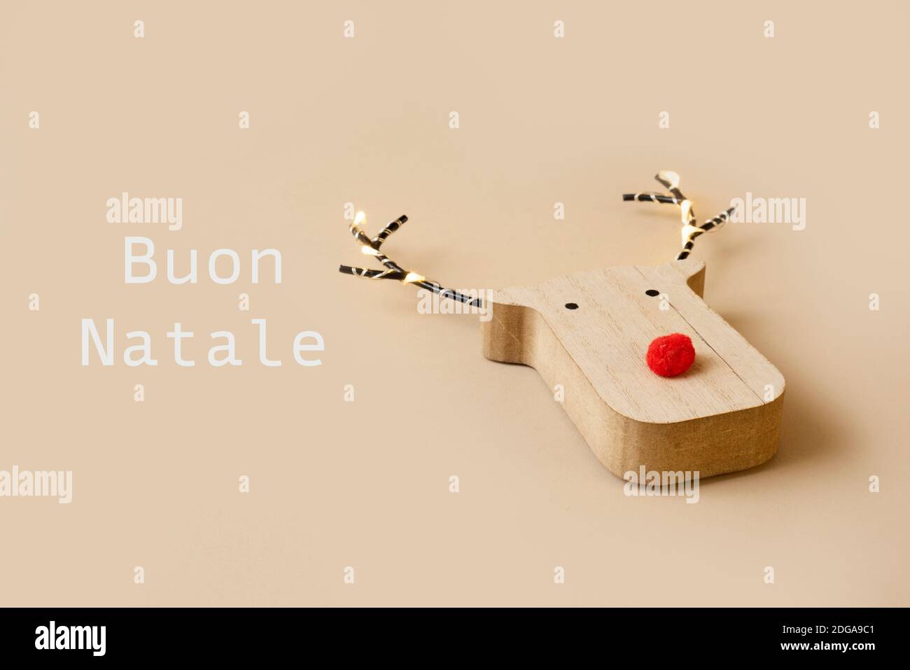 une tête de renne en bois drôle, avec un nez rouge, et le texte joyeux noël en italien sur un fond marron pâle Banque D'Images