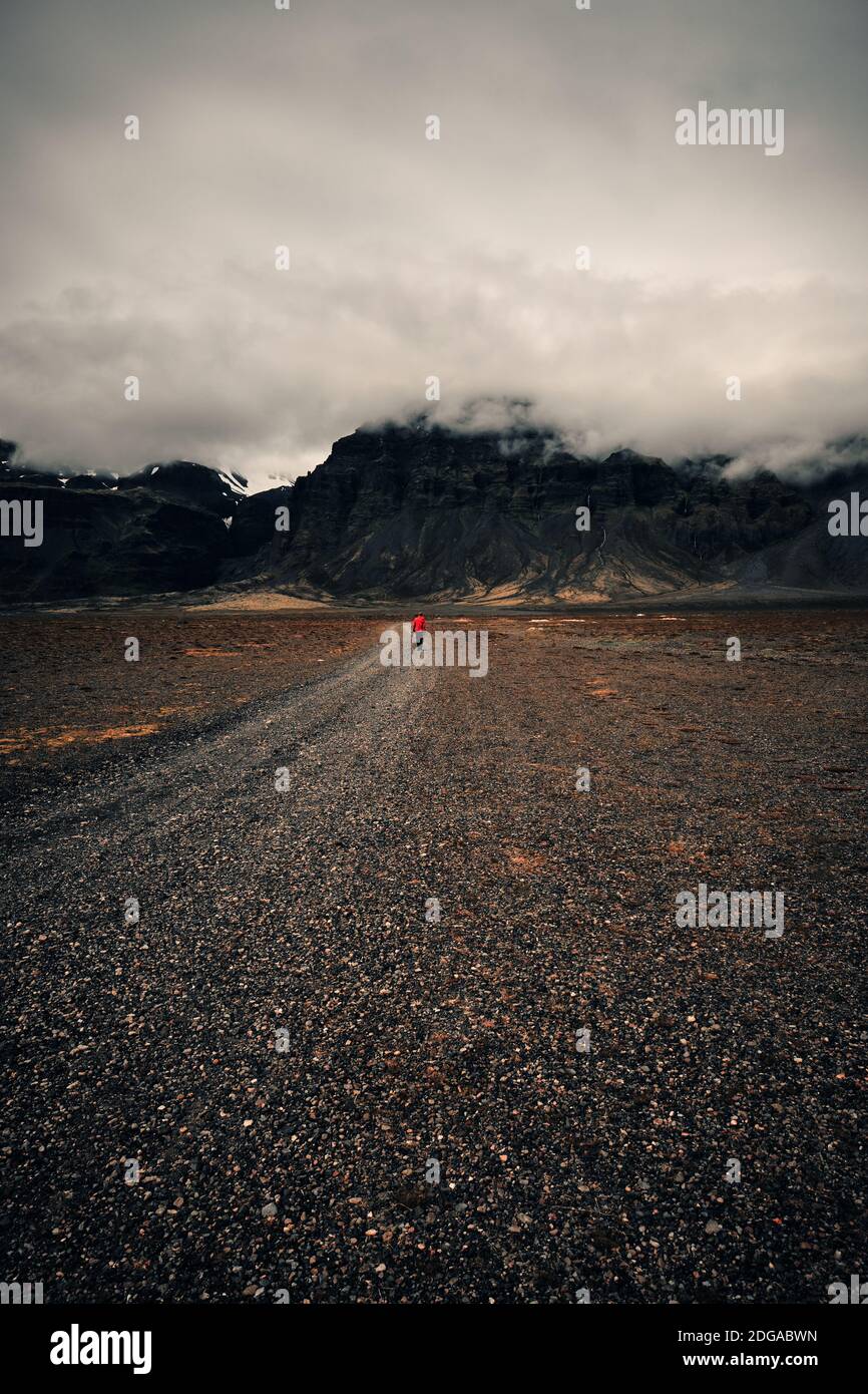 Un homme de randonnée solitaire dans les promenades rouges dans le bas cloud montagne isolée et plaine de lave rocheuse du sud Islande - Iceland ranker Banque D'Images