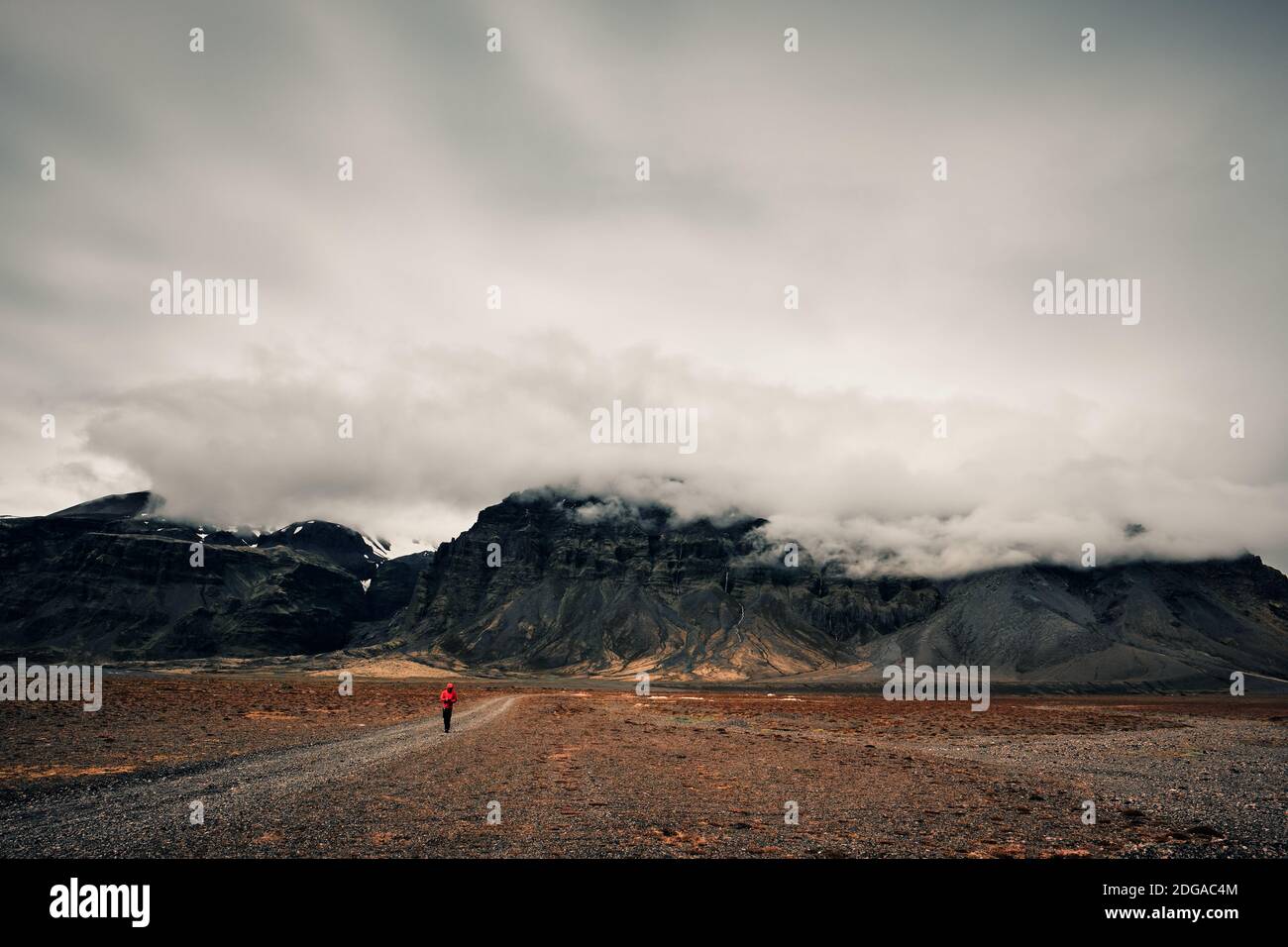 Un homme de randonnée solitaire dans les promenades rouges dans le bas cloud montagne isolée et plaine de lave rocheuse du sud Islande - Iceland ranker Banque D'Images