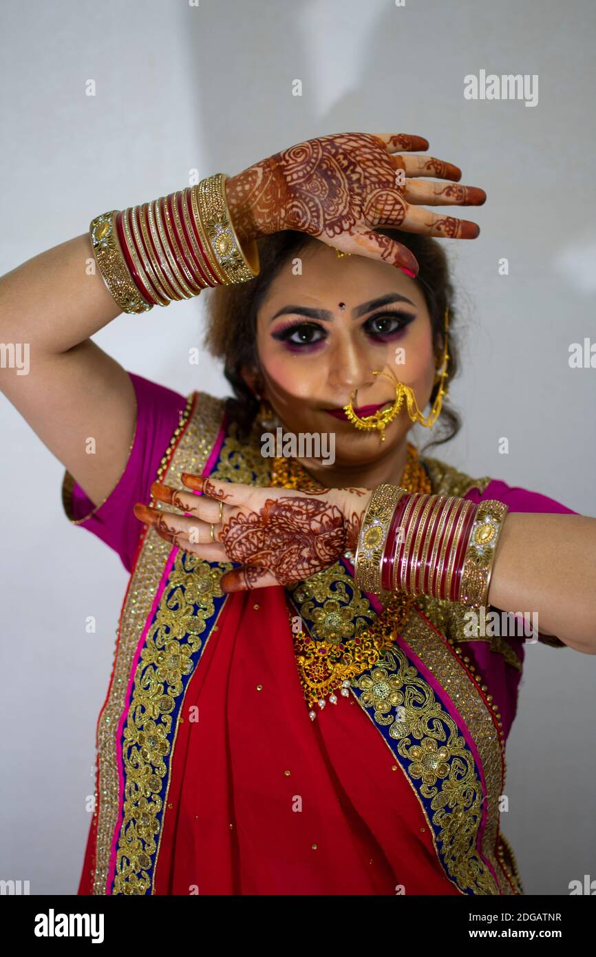 une belle fille indienne en robe de mariée portant une saree rouge et des ornements dorés montrant le tatouage appelé mehindi Banque D'Images