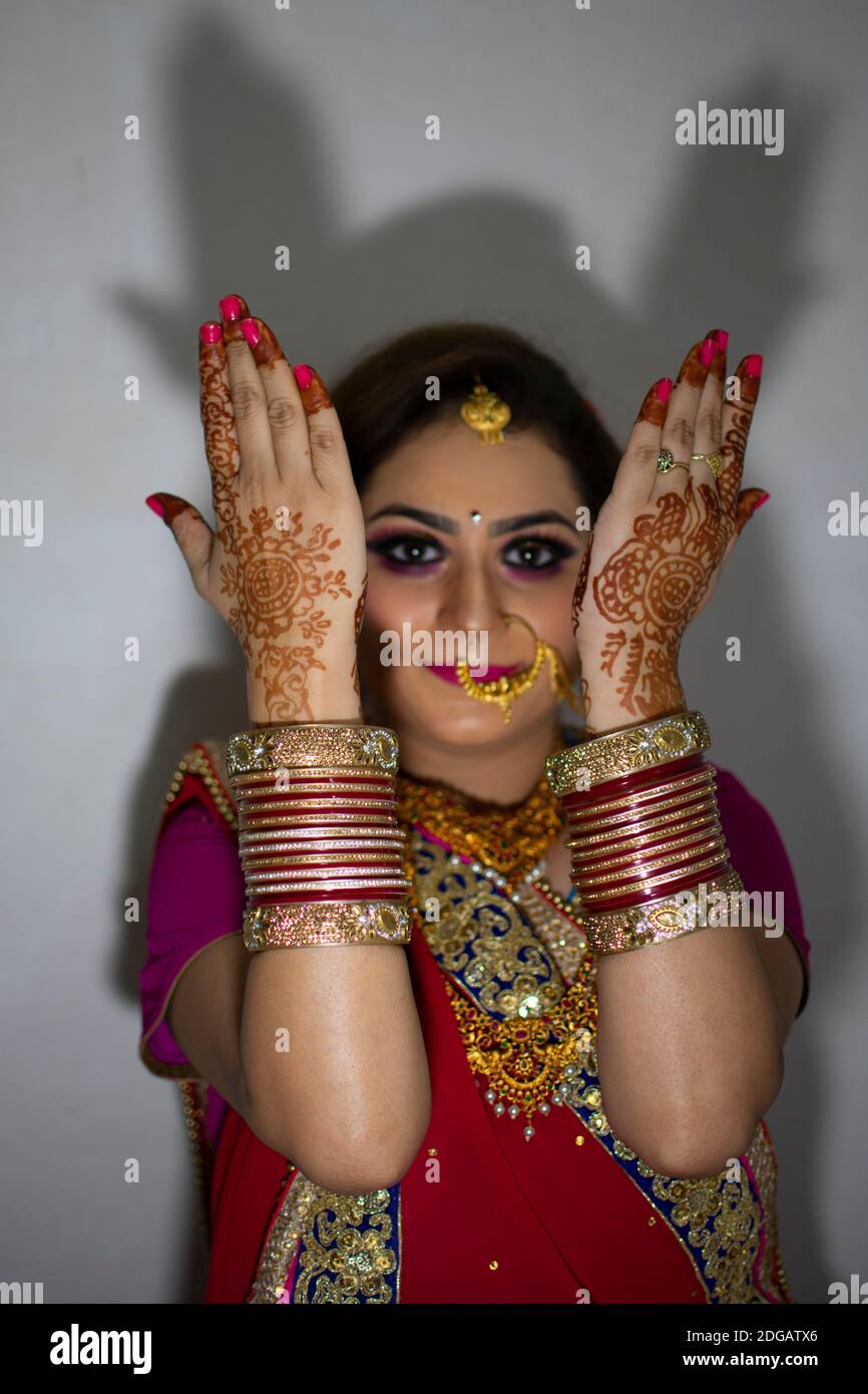 une belle fille indienne en robe de mariée portant une saree rouge et des ornements dorés montrant le tatouage appelé mehindi Banque D'Images