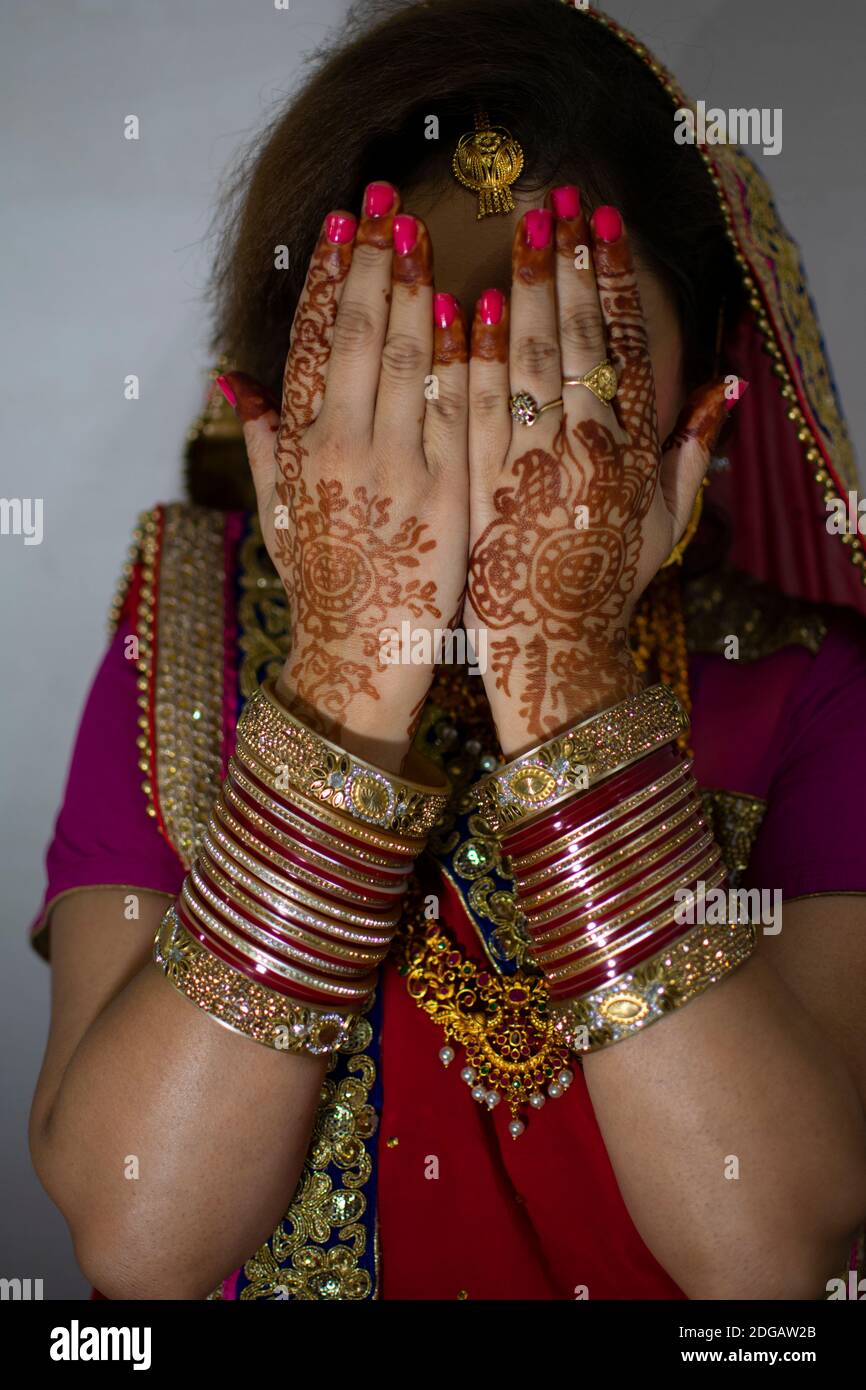 une belle fille indienne en robe de mariée portant une saree rouge et des ornements dorés montrant le tatouage appelé mehindi Banque D'Images