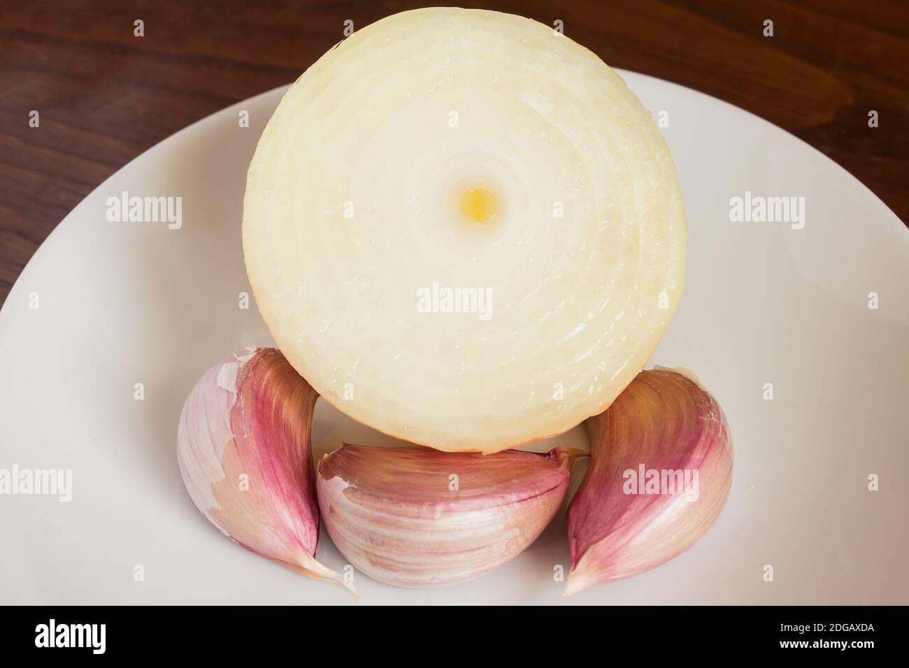 Un oignon coupé en deux et trois gousses d'ail sur une assiette blanche sur une table en bois. Saveurs alimentaires et végétales. Banque D'Images