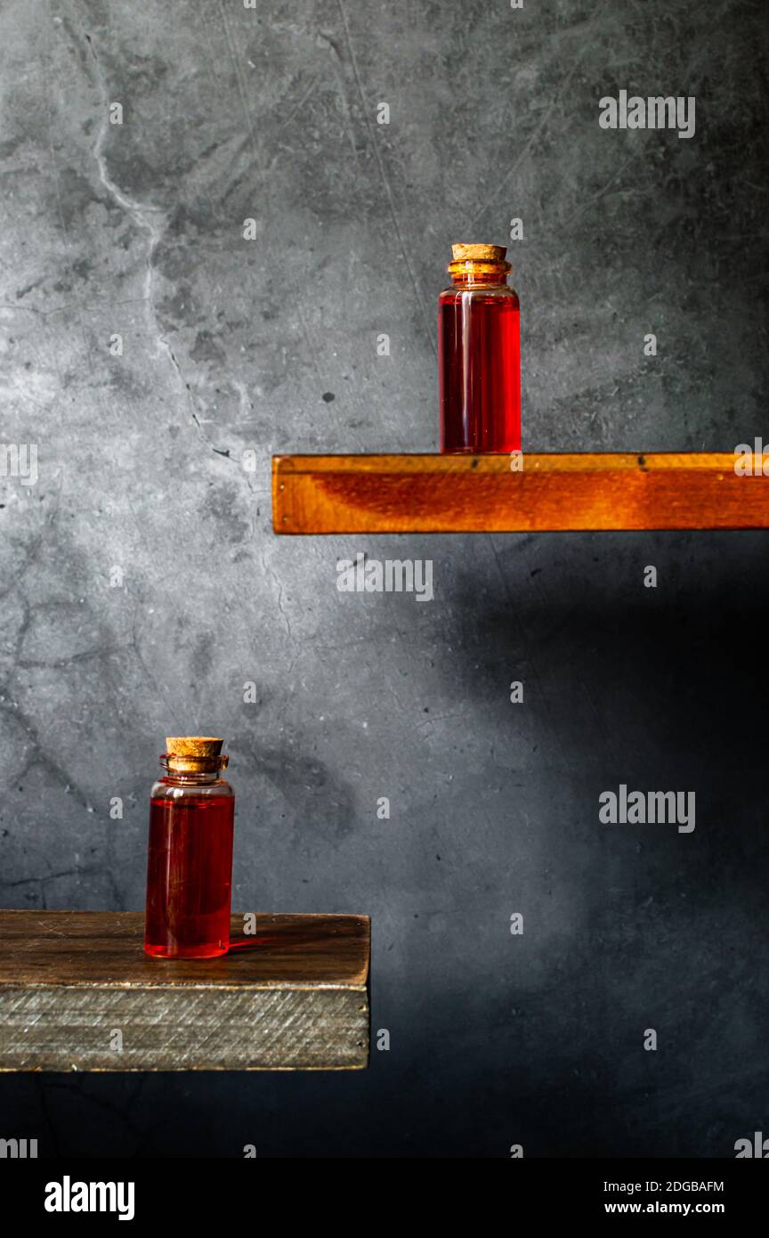 Deux flacons de bouchon en verre contenant du liquide rouge translucide sur du bois etagères sur fond texturé gris Banque D'Images