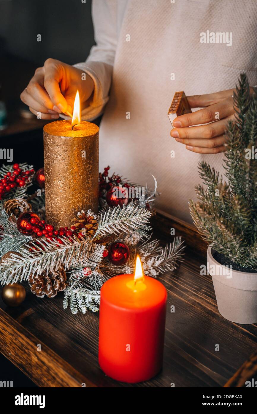 Bougies d'éclairage à la main pour femmes sur une table décorée à Noël.  Bougie nouvelle année brûlante, temps de l'avènement, lumières chaudes,  décorations d'hiver ornements sur le vieux r Photo Stock -