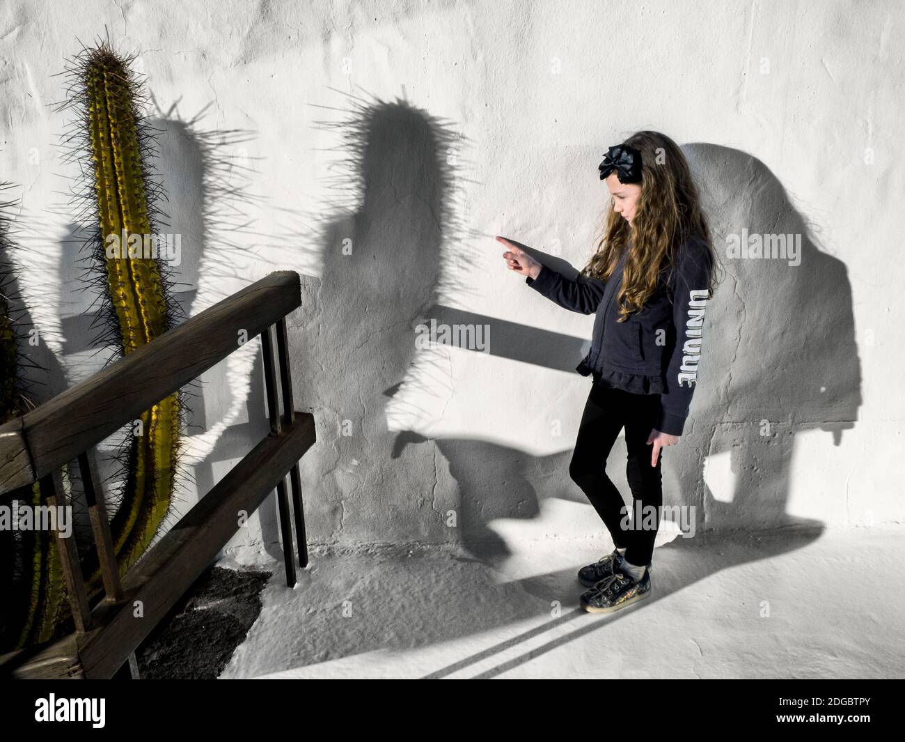 Fille debout près d'un mur touchant l'ombre d'un pic de cactus, Espagne Banque D'Images