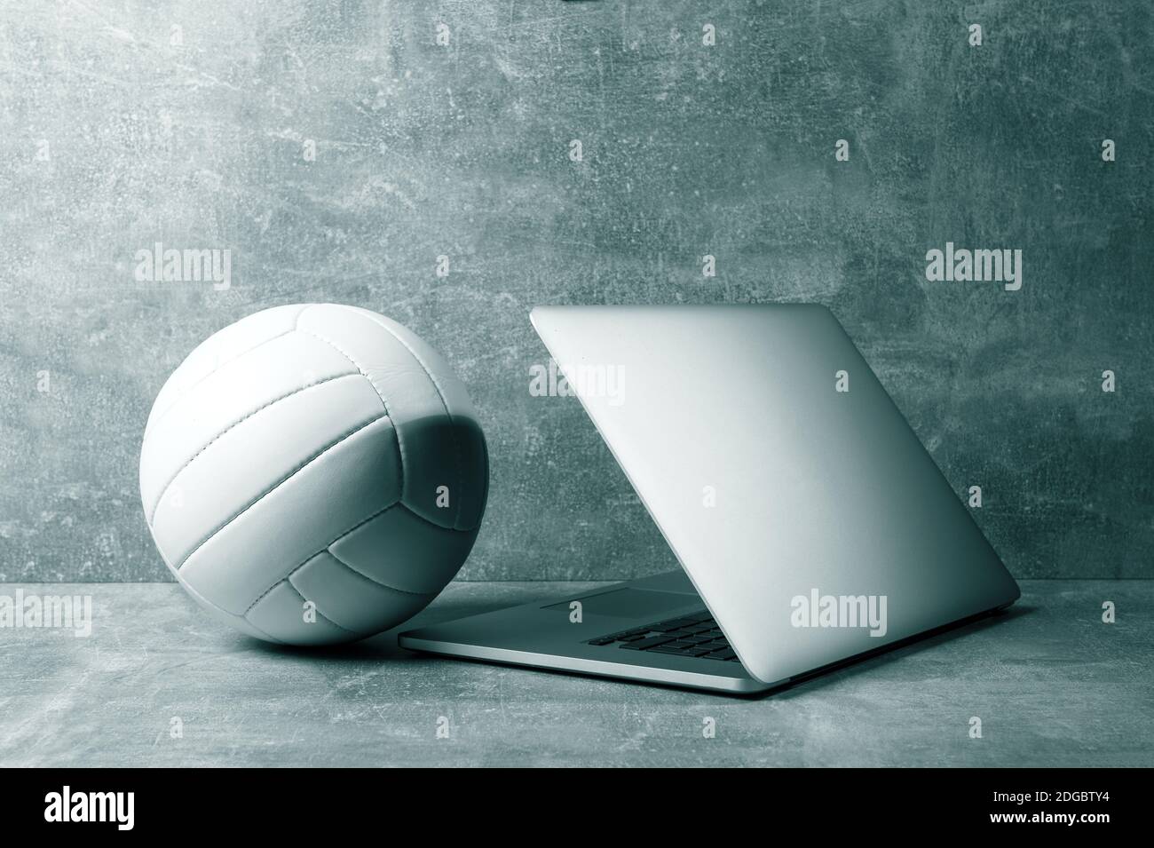 Ballon de volley-ball blanc et ordinateur portable gris sur fond gris. Concept d'entraînement en ligne. Filtre de couleur vert Banque D'Images