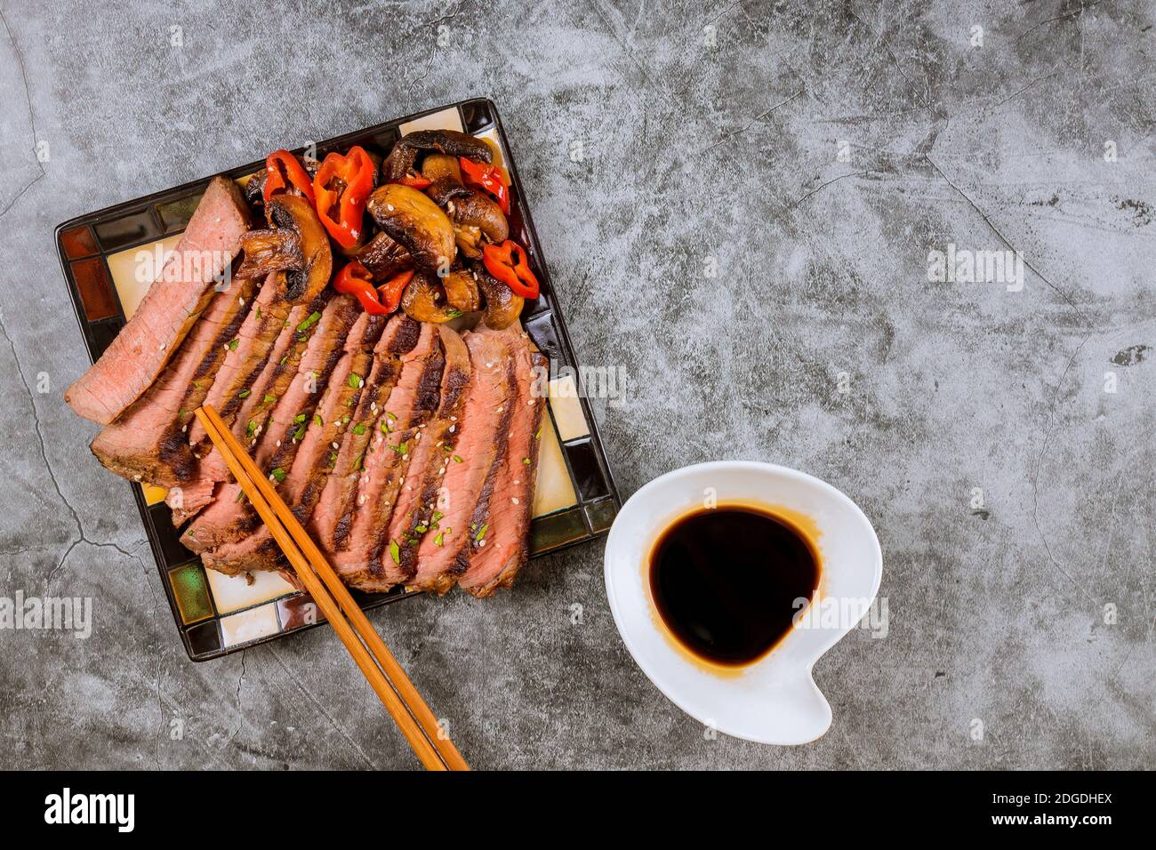 Bœuf rôti de bœuf coréen fait de la sirloin mince de steak frit dans les poivrons rouges et les champignons sur l'assiette avec des baguettes Banque D'Images