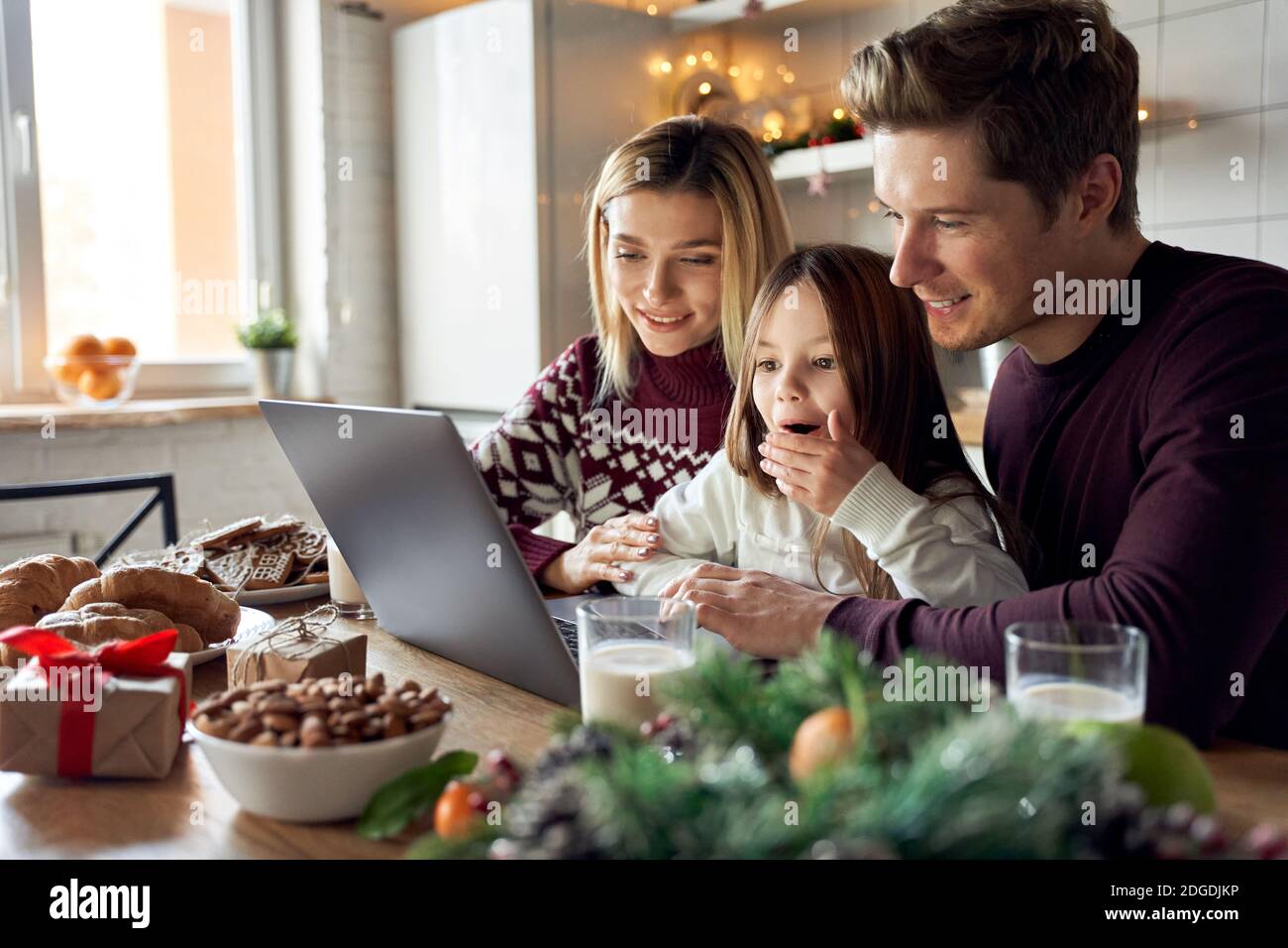 Parents heureux avec une fille enfant excitée utilisant un ordinateur portable assis à la table de Noël. Banque D'Images