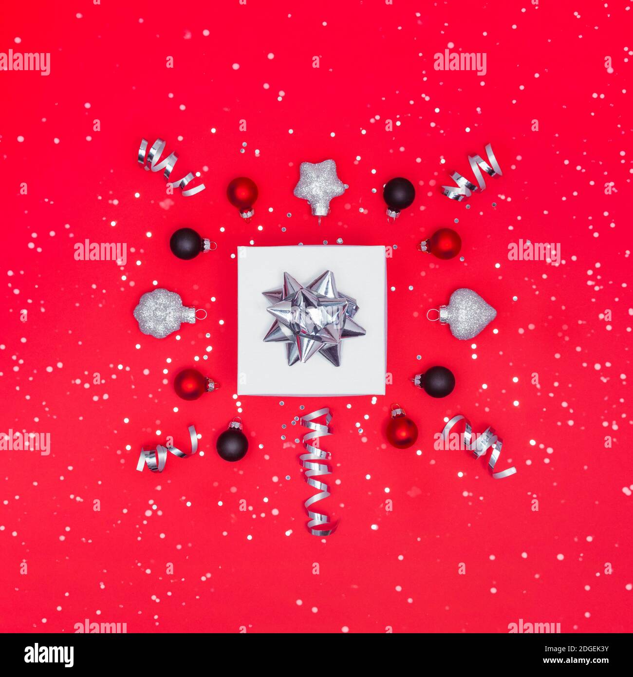 Boîte cadeau blanche avec décorations argentées, rouges et noires, confettis, neige et sparkles. Noël ou nouvel an présent. Pose avec espace de copie Banque D'Images
