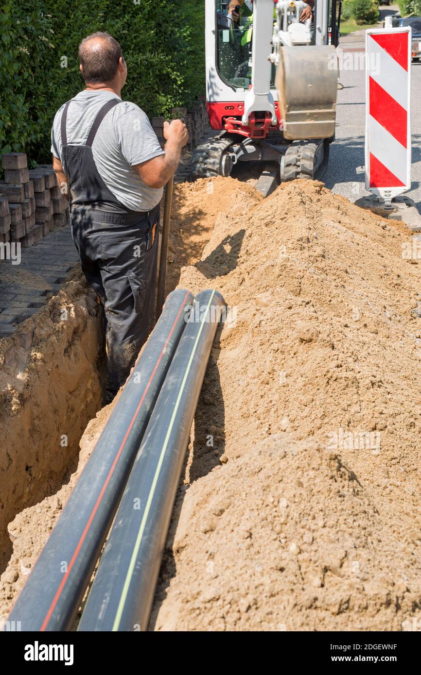 Travailleurs qui installent des câbles en fibre optique tranchées excavées par la machine de pelle hydraulique. Banque D'Images