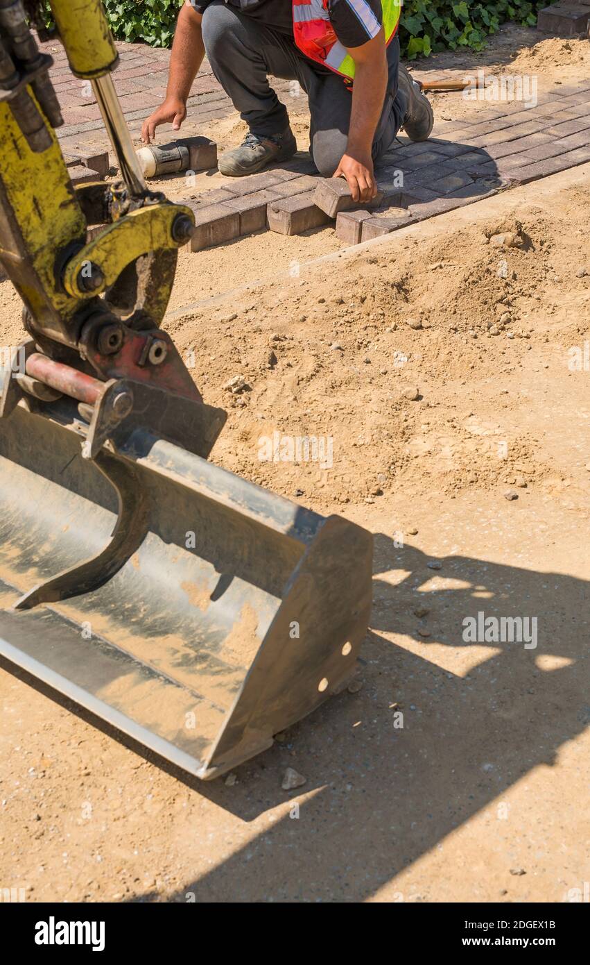 L'ouvrier pose des pierres de pavage en couches, en utilisant un marteau pour solidifier les pierres sur le sol pour réparer le trottoir piétonnier à côté de la rue. Banque D'Images