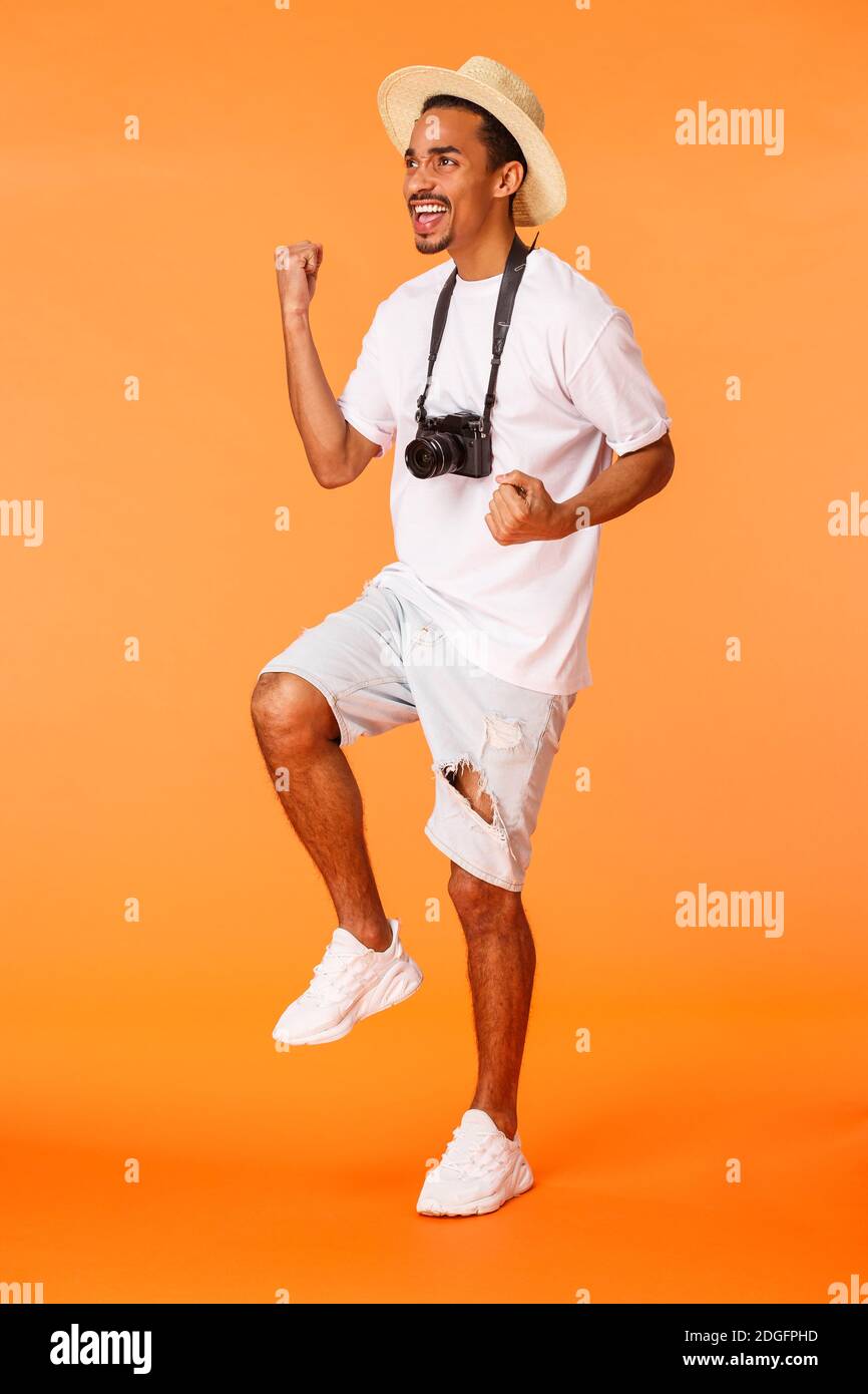 Homme de tir vertical sur toute la longueur debout dans le terminal de l'aéroport portant un short, un t-shirt blanc, une pompe de poing triomphante et une empeigne Banque D'Images