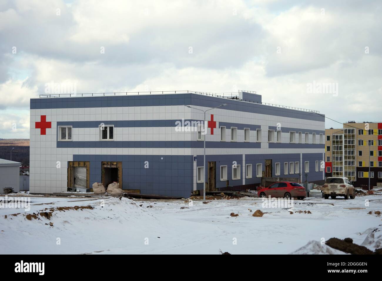 Des voitures se trouvent près du bâtiment de l'hôpital de la ville en cours de construction sur un site de projet par une journée d'hiver nuageux. Banque D'Images