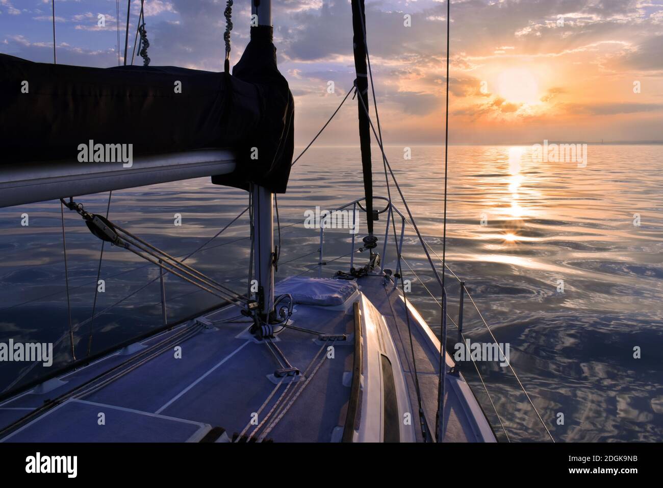 Voilier sur mer calme pendant le coucher du soleil avec des ciels orange et rose Banque D'Images
