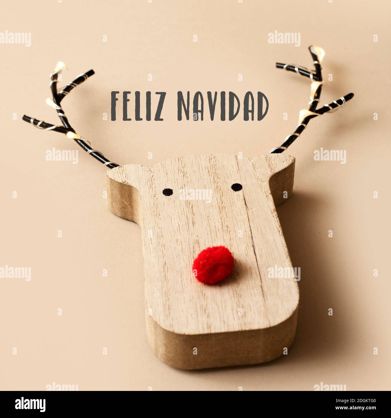 une tête de renne en bois drôle, avec un nez rouge, et le texte joyeux noël en espagnol sur un fond brun pâle Banque D'Images