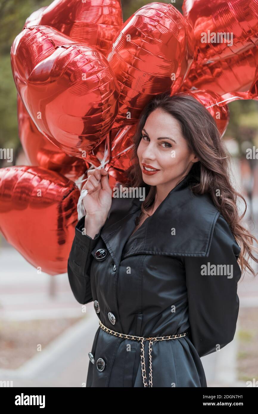 Le joli modèle hispanique de Brunette célèbre la Saint Valentin avec une douzaine Ballons cœur rouge Banque D'Images