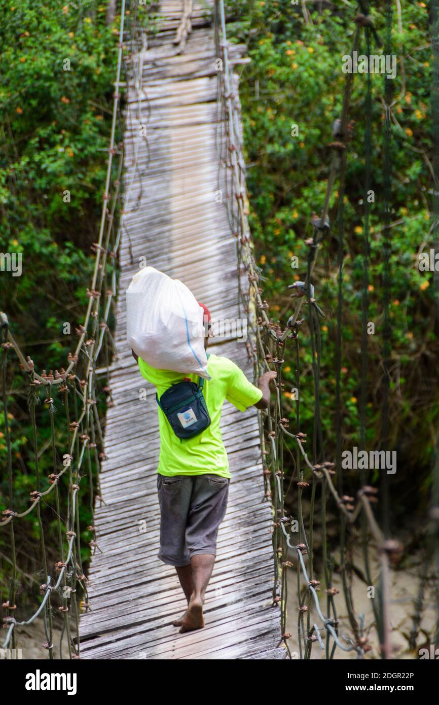 Porter porte un sac sur son épaule tout en traversant un pont suspendu fragile dans la vallée de Baliem, en Papouasie occidentale, en Indonésie. Banque D'Images