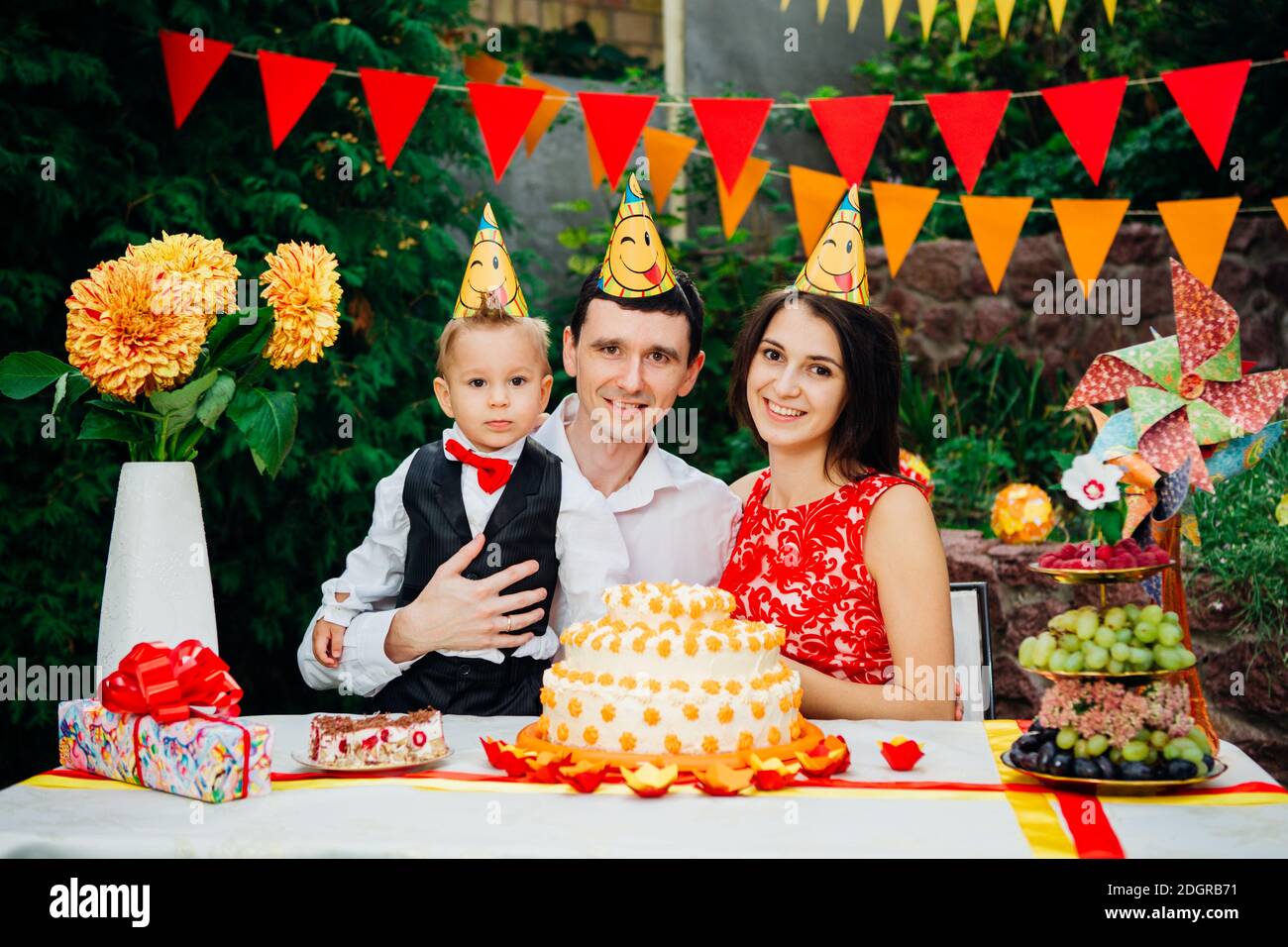 Thème anniversaire enfants. Famille de trois personnes caucasiennes assis dans l'arrière-cour de la maison à une table festive décorée dans drôle Banque D'Images