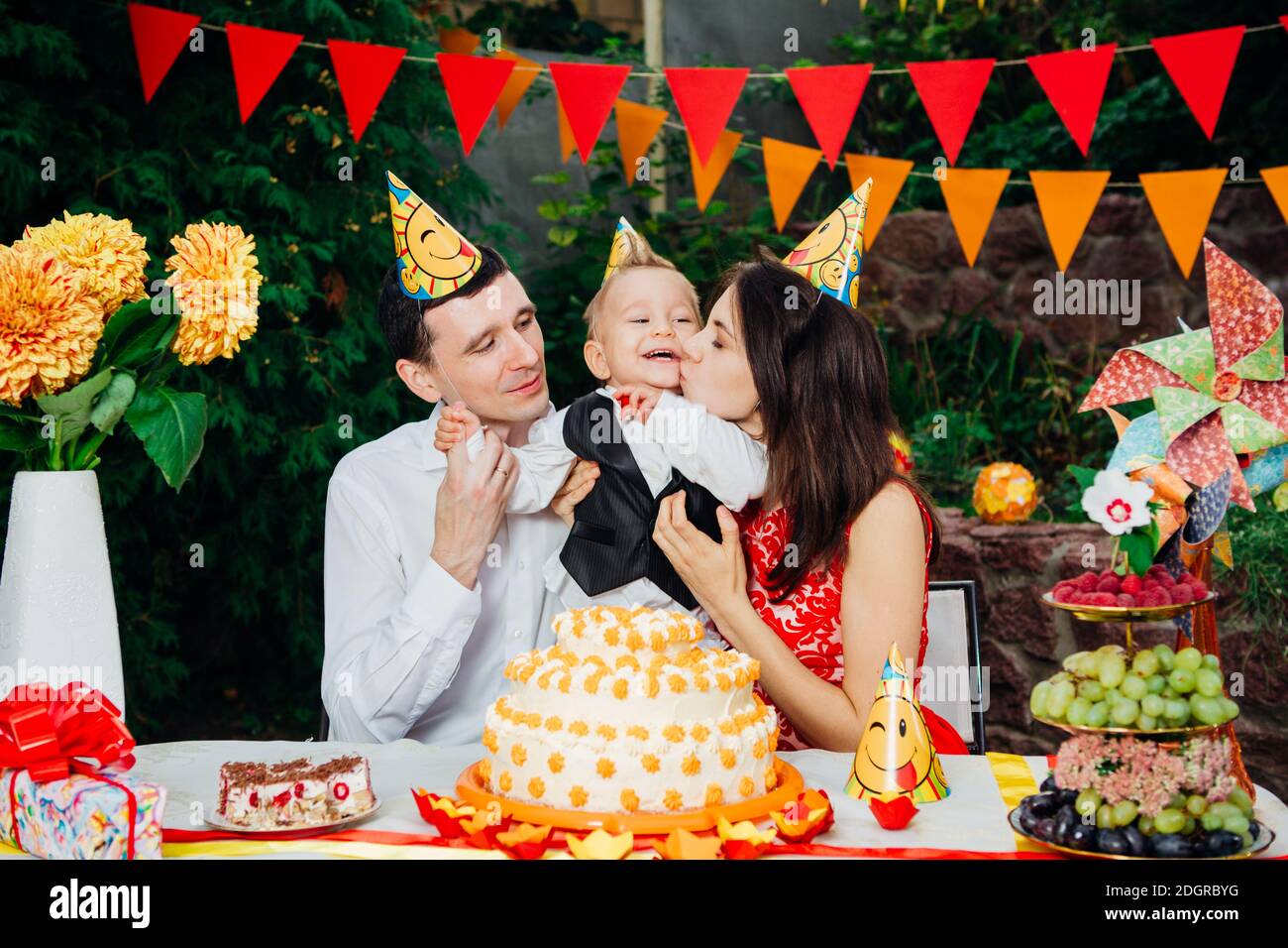 Thème anniversaire enfants. Famille de trois personnes caucasiennes assis dans l'arrière-cour de la maison à une table festive décorée dans drôle Banque D'Images