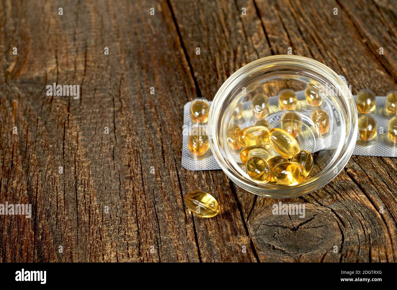 Capsules d'huile de poisson dans un bol en verre sur fond de bois ancien Banque D'Images