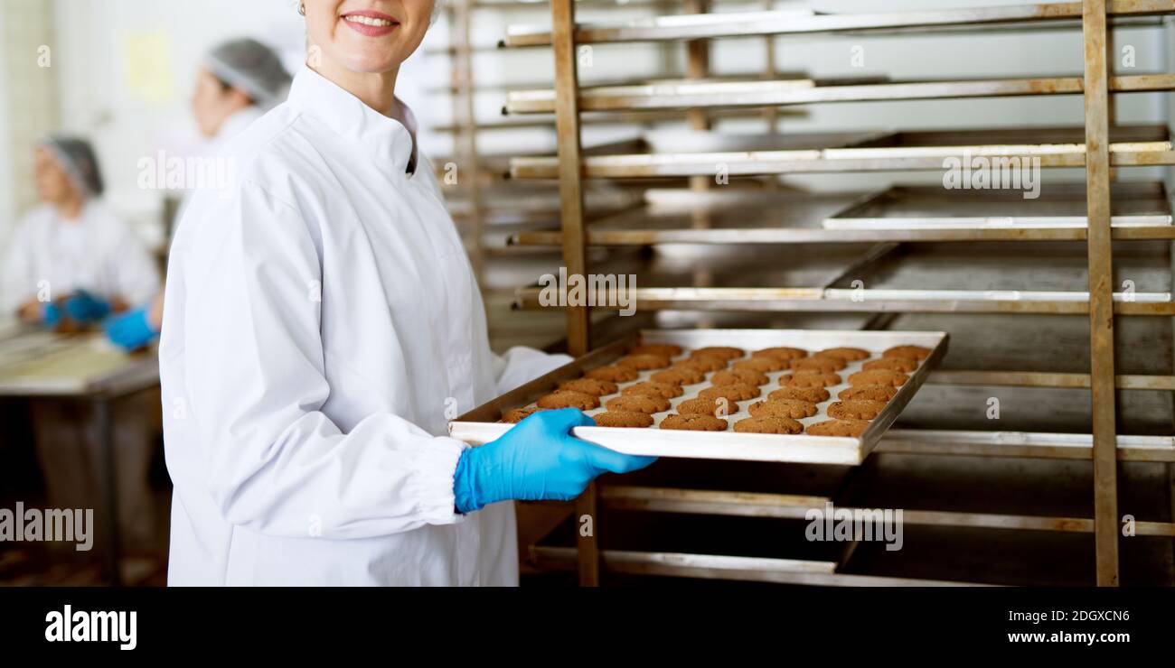 Des biscuits fraîchement cuits placés sur un moule pour refroidir sont placés sur une étagère par une travailleuse. Banque D'Images