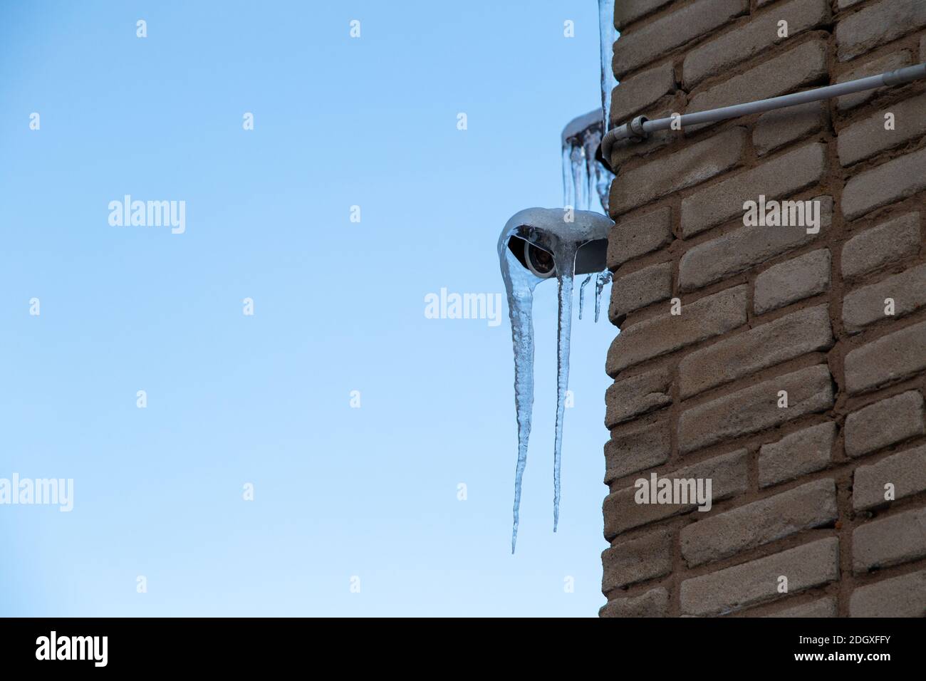 Une caméra de surveillance de la rue fixée à un mur de briques est fortement givrée, les glaçons pendent. Banque D'Images