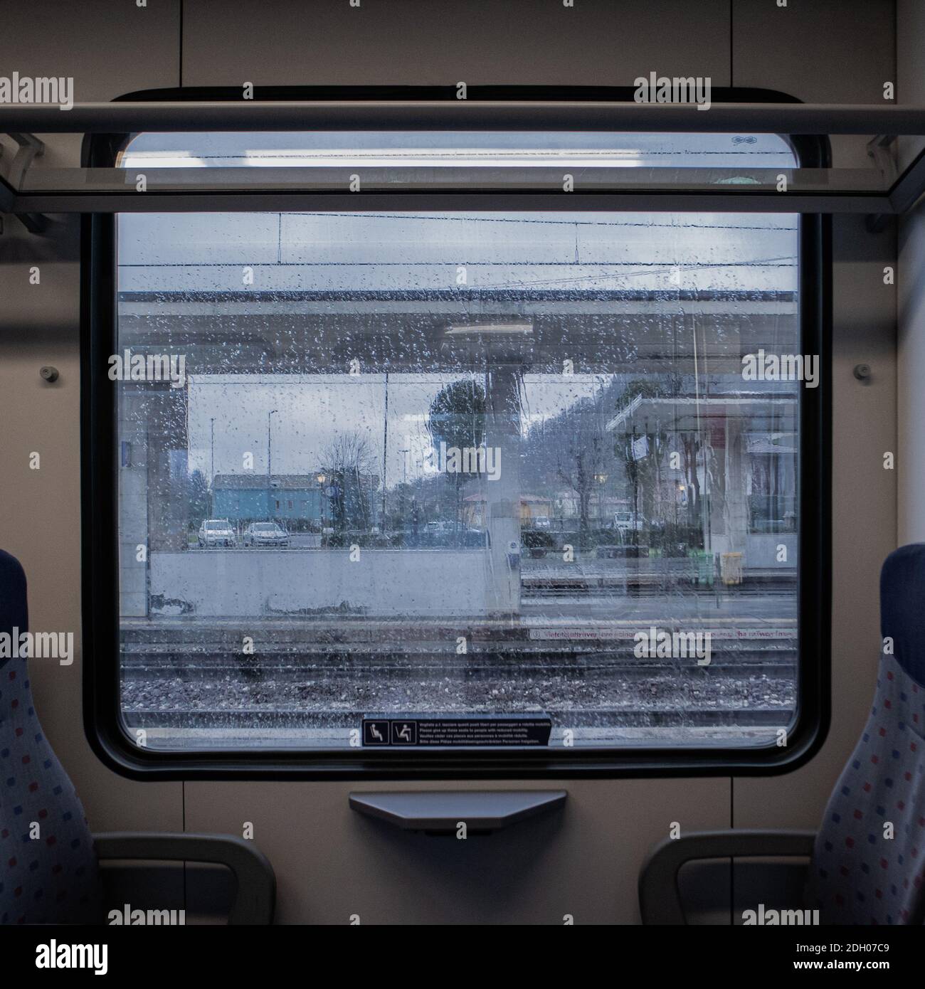 une fenêtre carrée dans un autocar de train pendant un pluvieux jour où vous pouvez voir la gare à l'extérieur Banque D'Images
