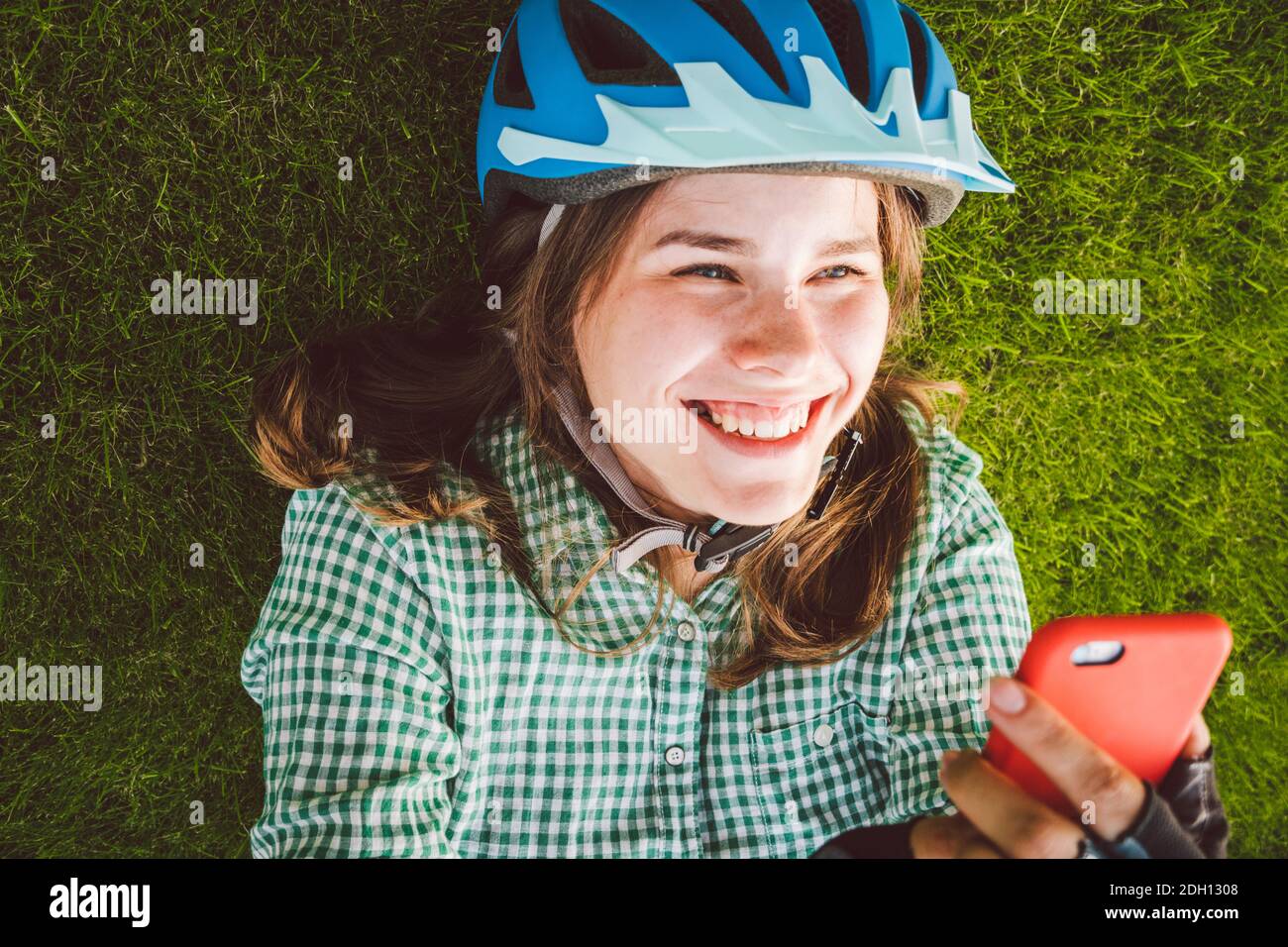 Thème sport et technologie. Belle femme caucasienne étudiant avec un sourire Toothy repose dos herbe verte de repos dans le casque de vélo hea Banque D'Images