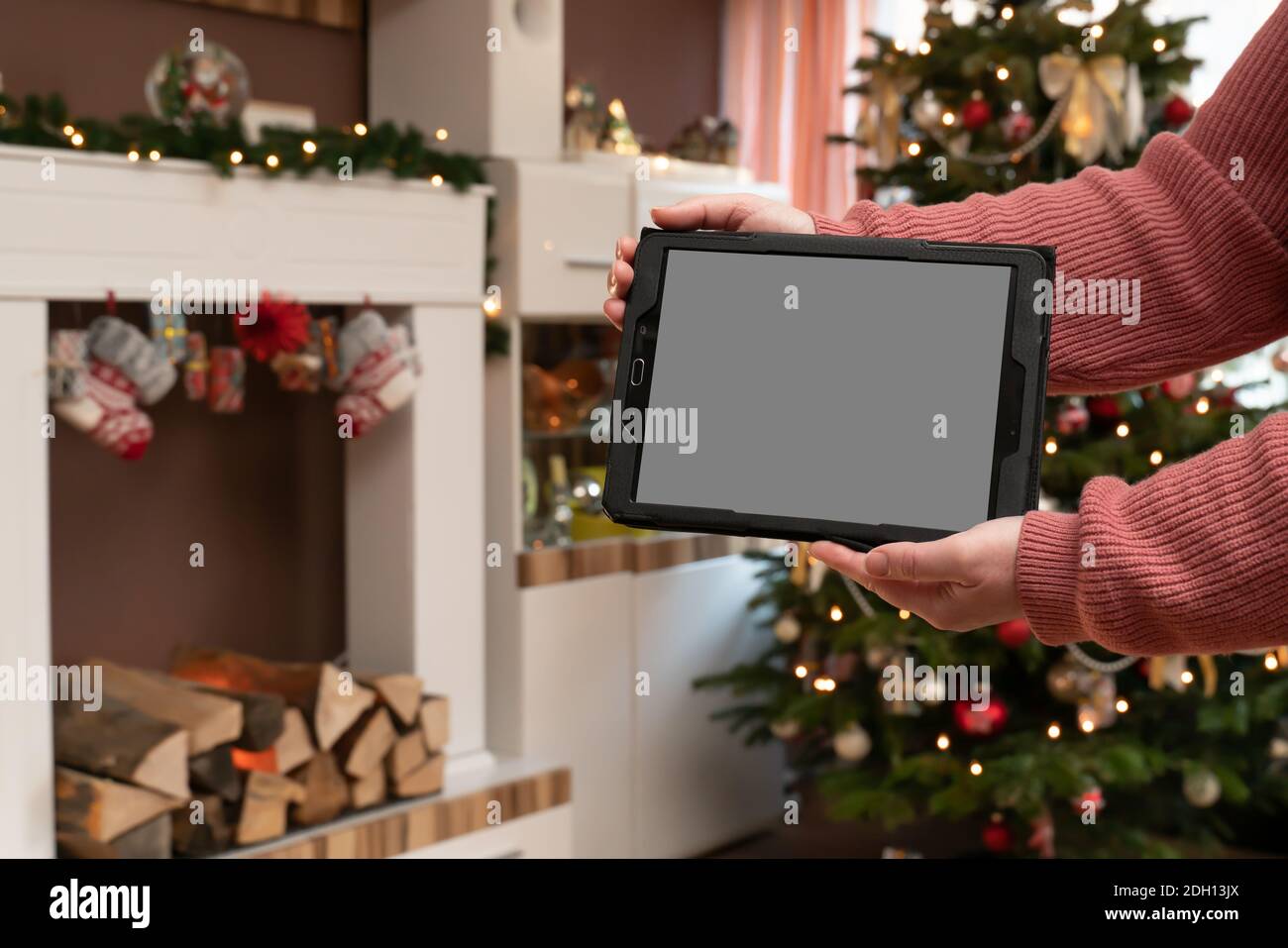 Les mains d'une femme ont une tablette PC. L'homme est debout dans un salon décoré de Christmassy. Console de l'arbre de Noël et de la cheminée. Banque D'Images